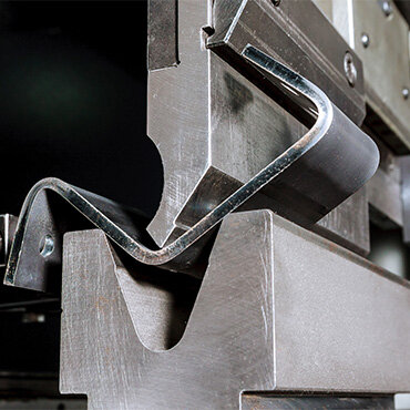 Close-up of a metal bending process using a press brake machine, shaping a sheet of metal into a precise curved form.